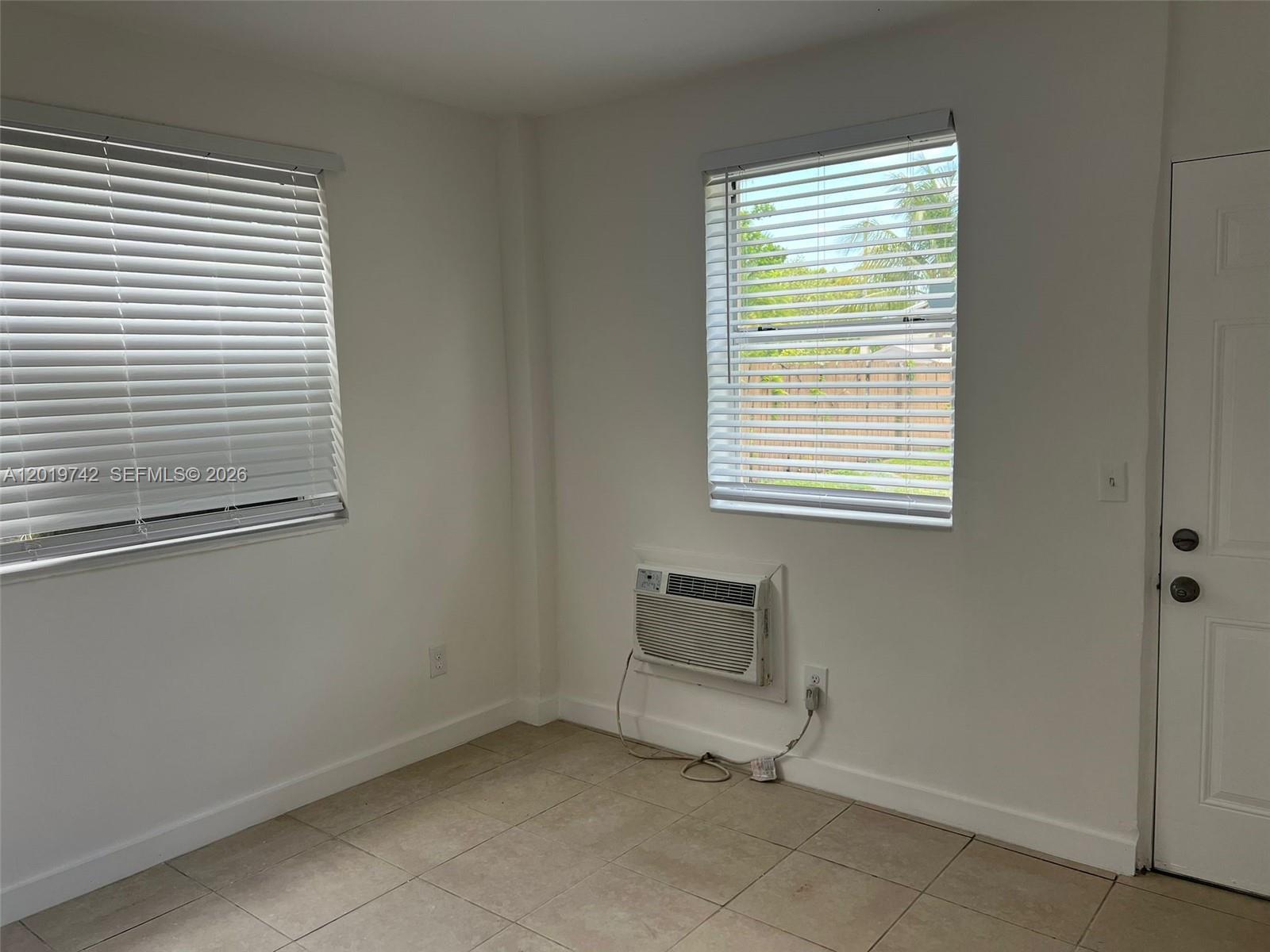 A room with white walls, tile flooring, two windows with blinds, and a wall-mounted air conditioner — 4245 NW 24th Ave # 1, Miami FL 33142, MIAMI, FL