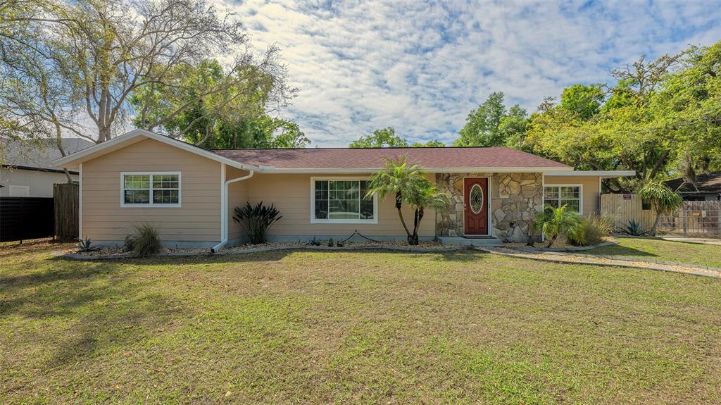 A single-story house with tan siding, a stone facade, and a red front door — 3818 GOCIO ROAD, SARASOTA, FL