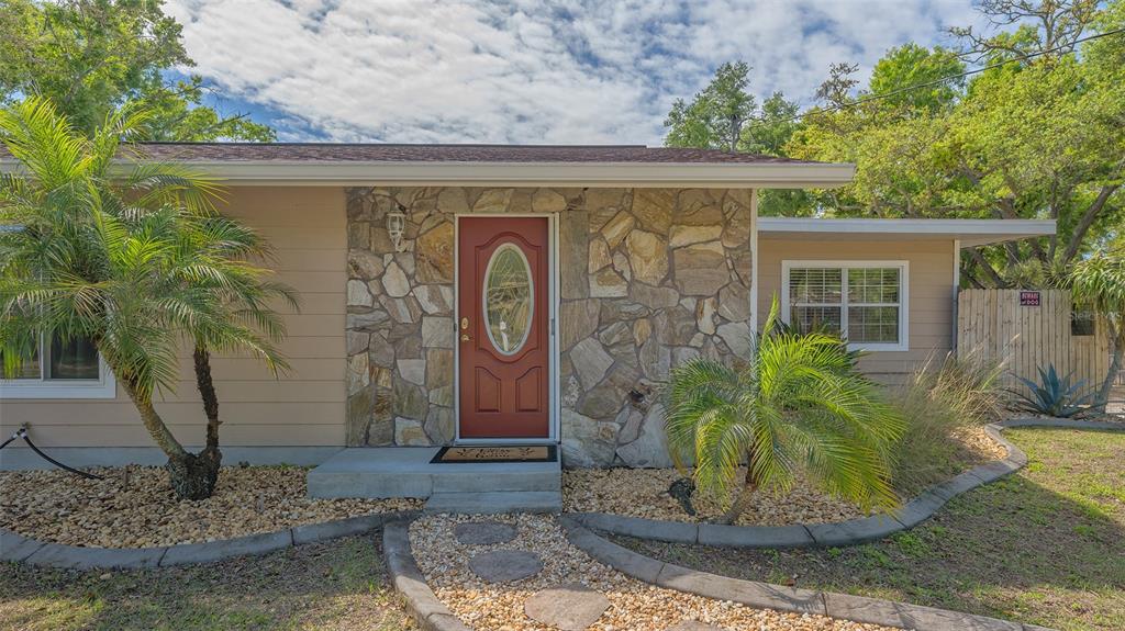 A single-story house with a stone facade, a red front door, and palm trees — 3818 GOCIO ROAD, SARASOTA, FL