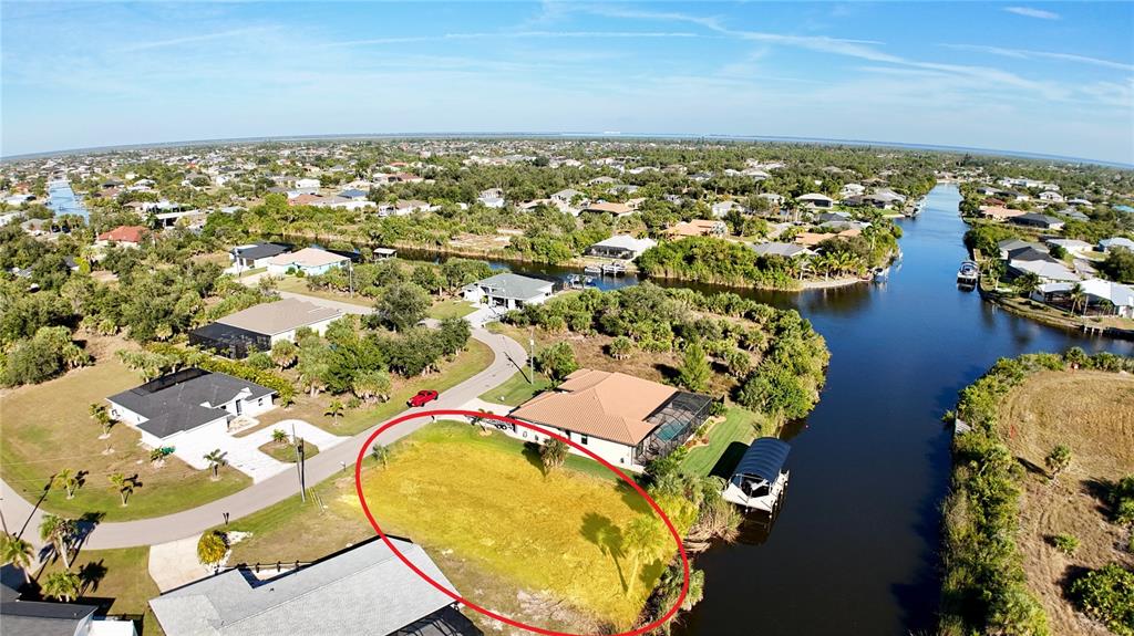 An aerial view shows a vacant, grass-covered residential lot situated along a canal — 9580 PRESIDENT CIRCLE, PORT CHARLOTTE, FL