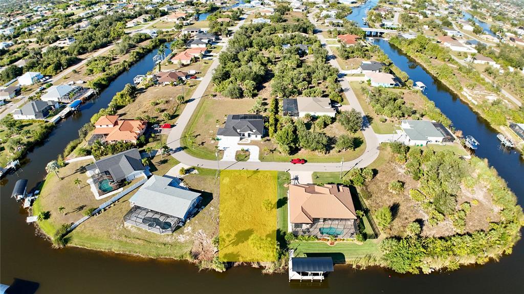 An aerial view shows a vacant waterfront lot highlighted in yellow between two residential homes — 9580 PRESIDENT CIRCLE, PORT CHARLOTTE, FL