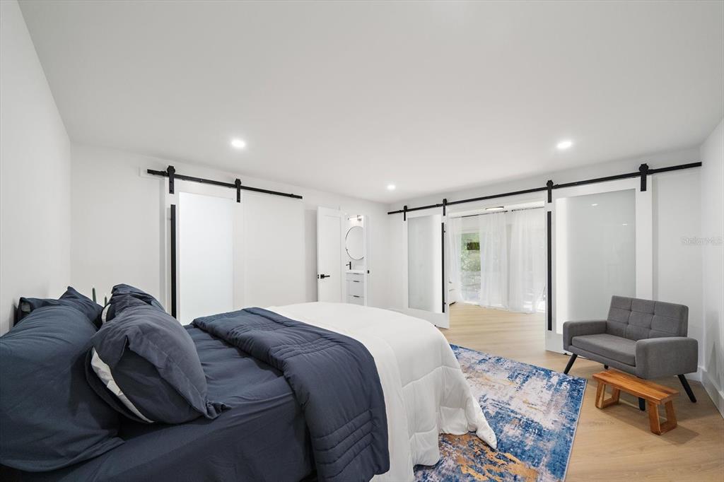 A bedroom features a bed, a gray chair, and sliding barn doors on white walls — 578 SPANISH DRIVE S, LONGBOAT KEY, FL