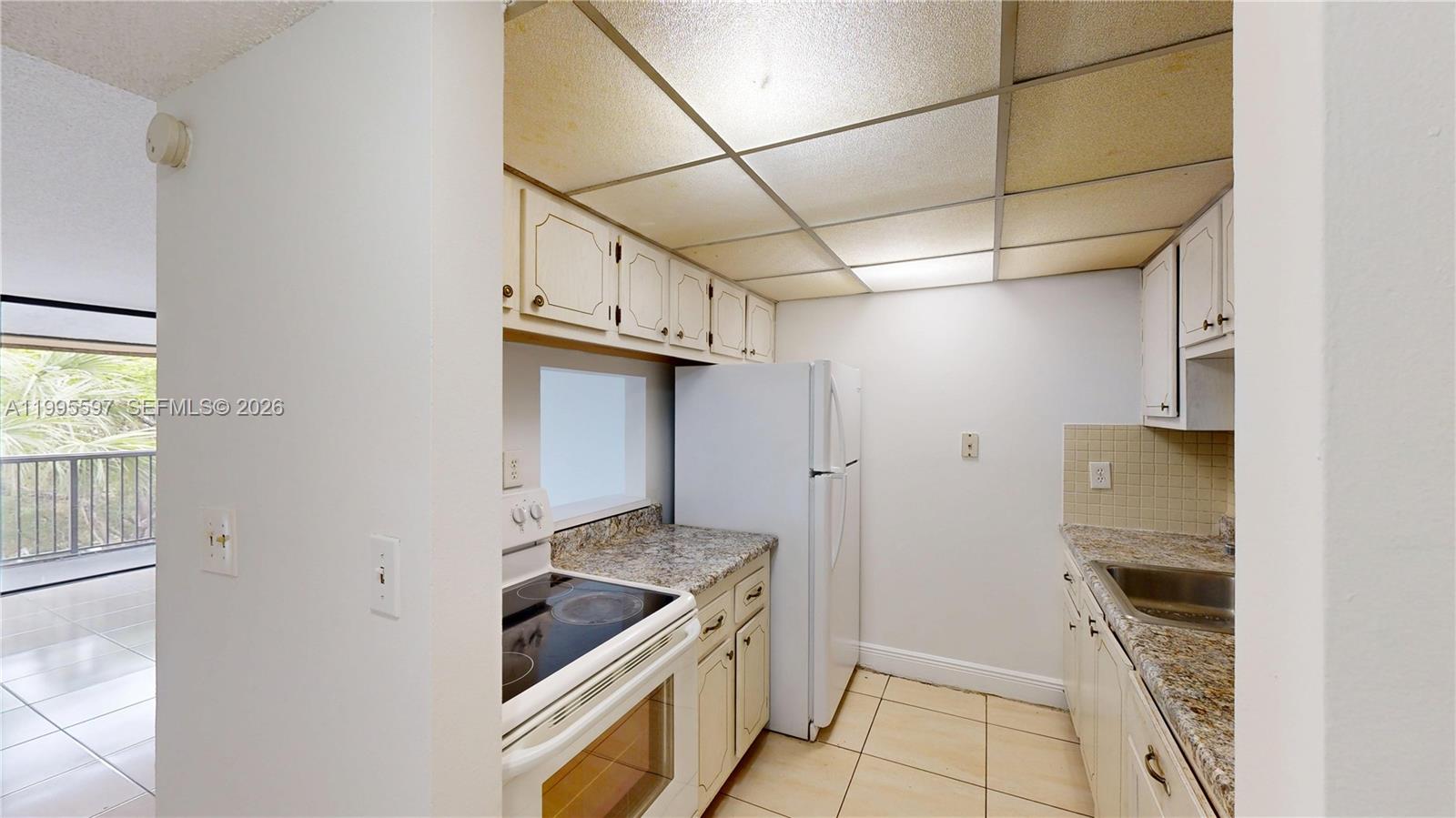 A galley kitchen features white cabinets, granite countertops, a white refrigerator, and a drop ceiling — 14201 N Kendall Dr # 401D, Miami FL 33186, MIAMI, FL