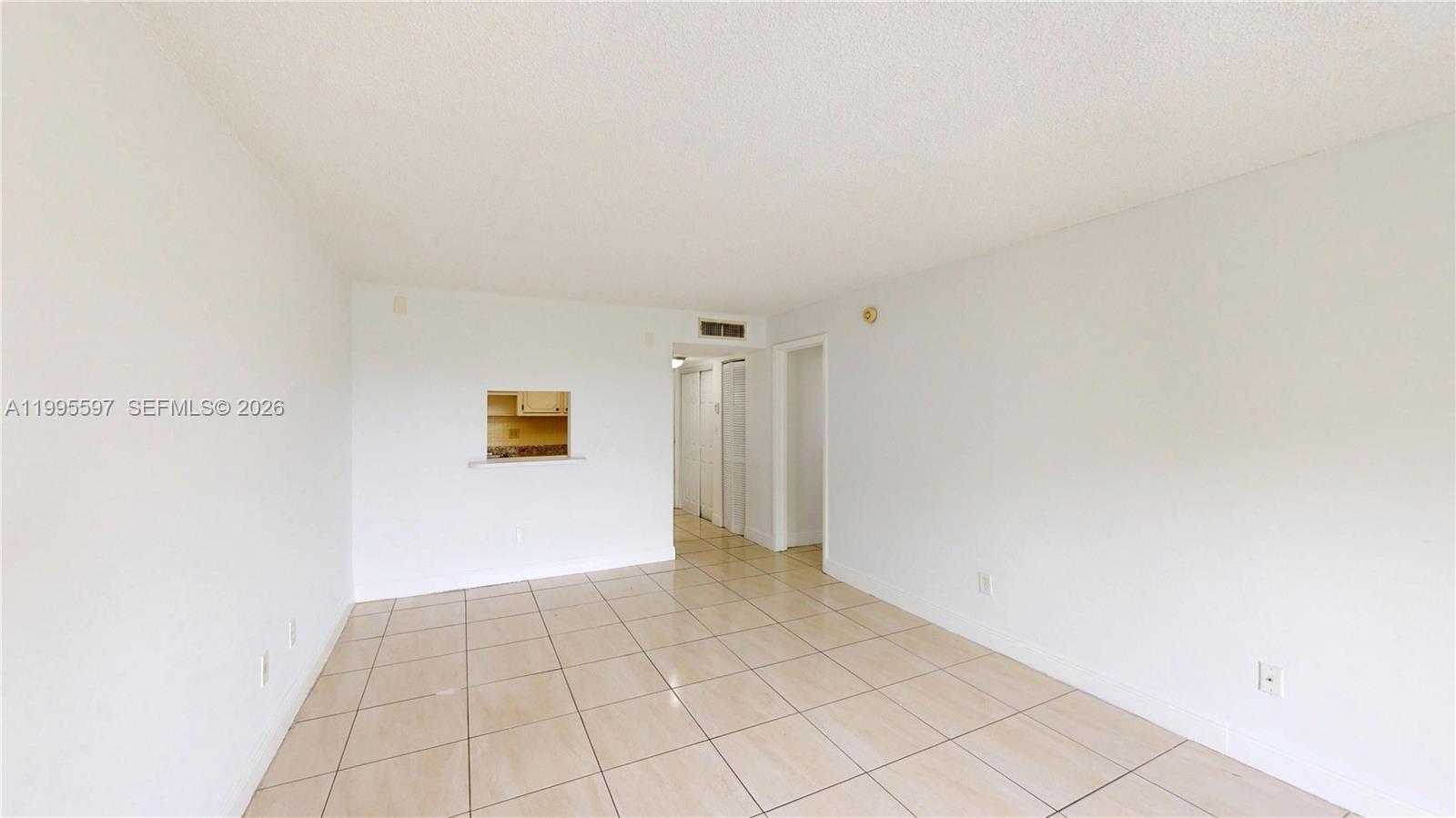 An empty room features white walls, light-colored tile flooring, and a kitchen pass-through window — 14201 N Kendall Dr # 401D, Miami FL 33186, MIAMI, FL