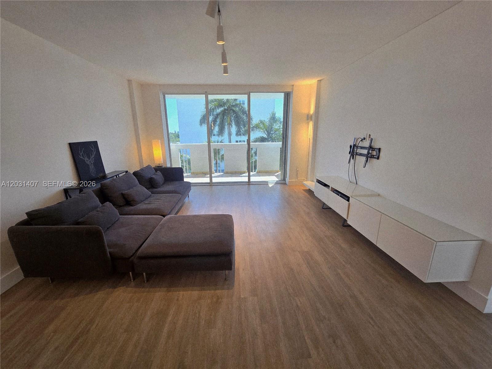 A living room features a dark gray sectional sofa, white media console, and balcony access — 800 West Ave # 618, Miami Beach FL 33139, MIAMI BEACH, FL