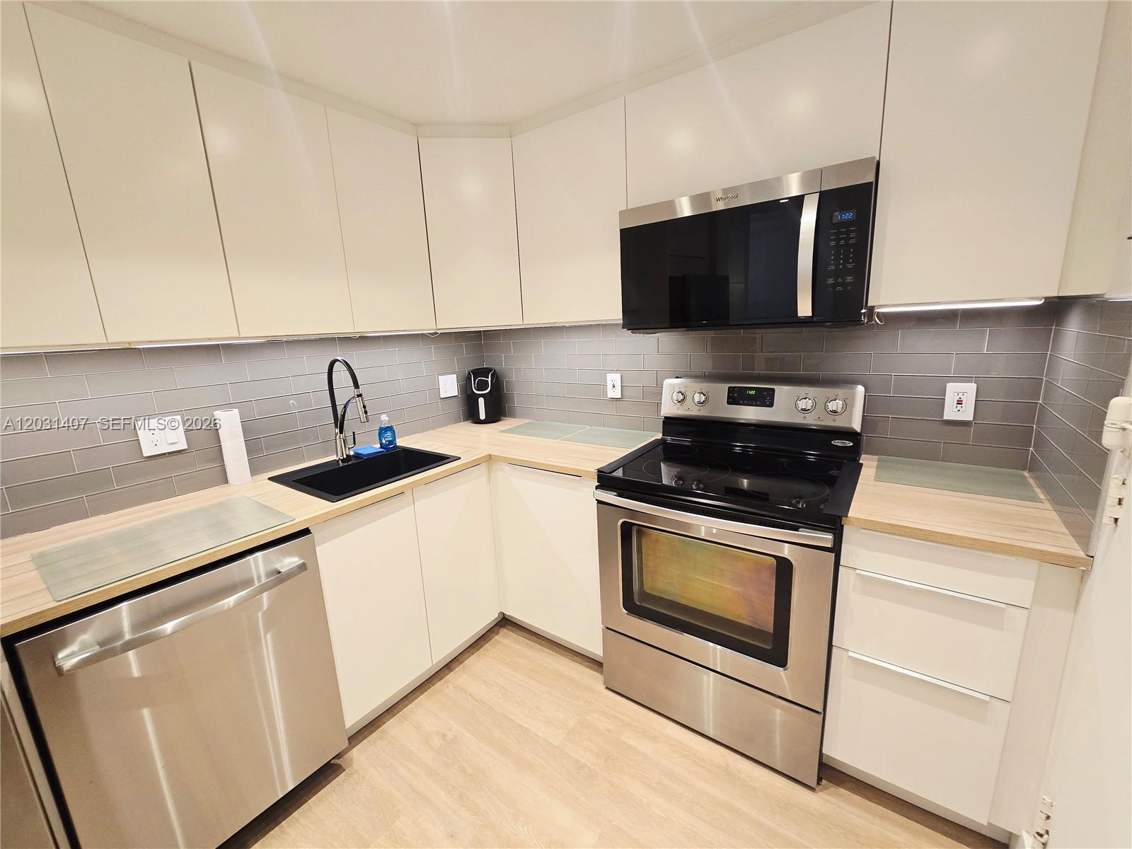 A modern kitchen features white cabinets, stainless steel appliances, a gray tile backsplash, and wood countertops — 800 West Ave # 618, Miami Beach FL 33139, MIAMI BEACH, FL