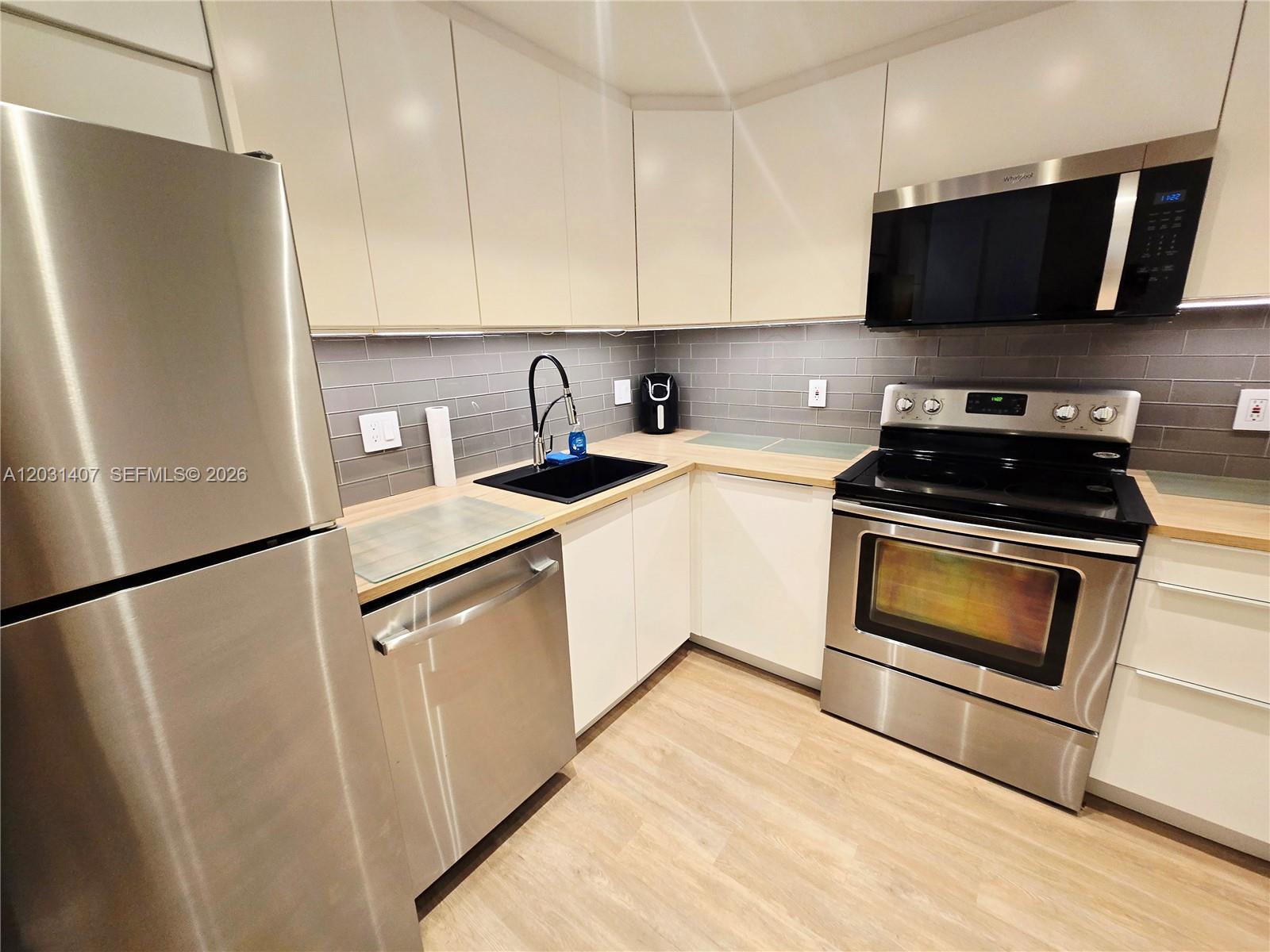 A modern kitchen features stainless steel appliances, white cabinets, and a gray tiled backsplash — 800 West Ave # 618, Miami Beach FL 33139, MIAMI BEACH, FL