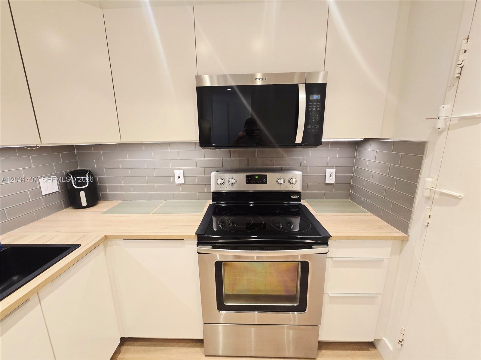 A kitchen features white cabinets, a stainless steel stove, a microwave, and a gray backsplash — 800 West Ave # 618, Miami Beach FL 33139, MIAMI BEACH, FL