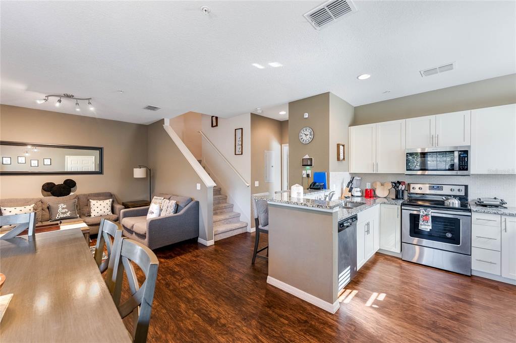 An open-concept kitchen and living area with wood flooring, white cabinets, and a staircase — 3212 CUPID PLACE, KISSIMMEE, FL