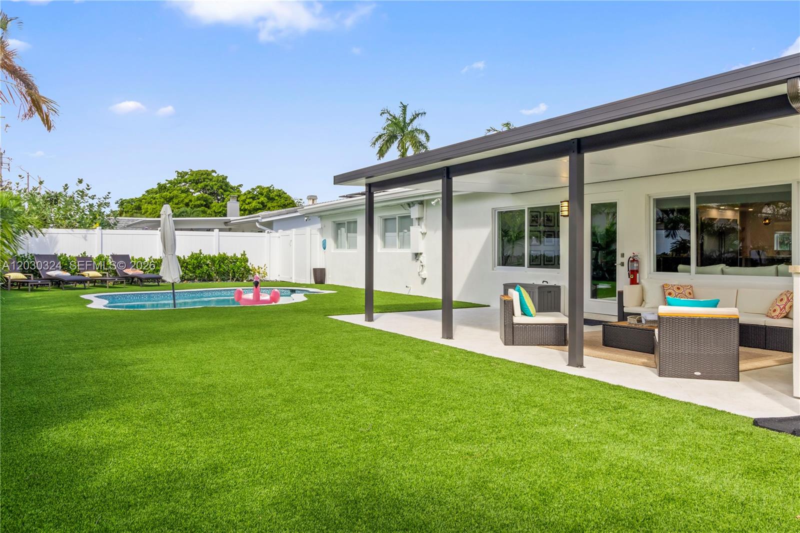 A backyard features a swimming pool, artificial turf, and a covered patio with outdoor furniture — 2862 NE 35th Ct, Lighthouse Point FL 33064, LIGHTHOUSE POINT, FL