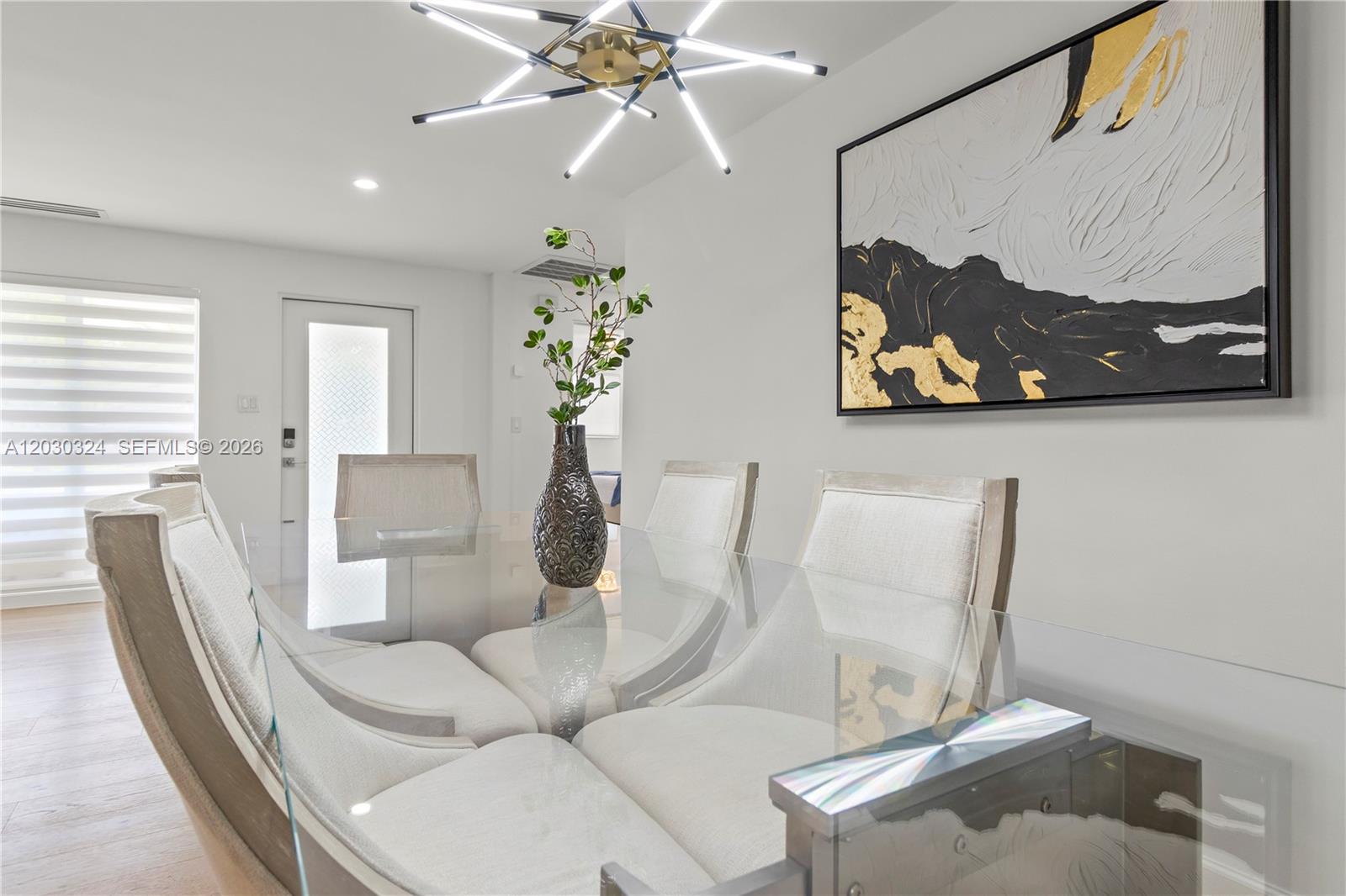A dining room features a glass table, upholstered chairs, a modern chandelier, and abstract art — 2862 NE 35th Ct, Lighthouse Point FL 33064, LIGHTHOUSE POINT, FL