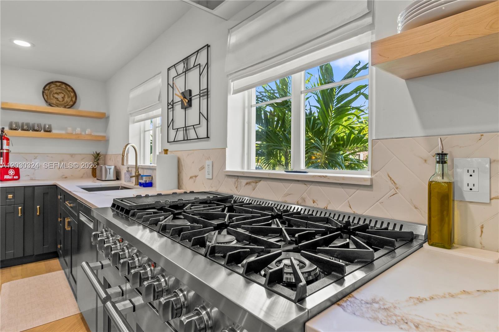 A kitchen features a large stainless steel gas range, marble-style backsplash, and open wood shelving — 2862 NE 35th Ct, Lighthouse Point FL 33064, LIGHTHOUSE POINT, FL