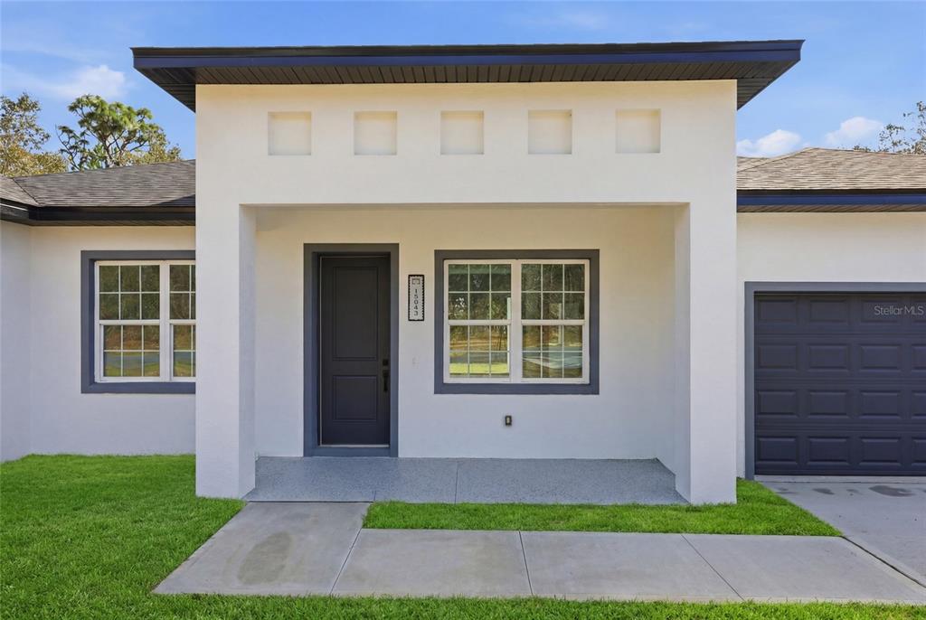 The exterior of a white house features a dark front door, garage, and concrete walkway — 15043 SW 60TH TERRACE, OCALA, FL