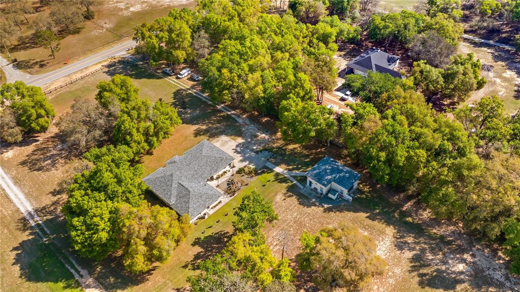 An aerial view shows a house, a detached garage, and a driveway amidst wooded acreage — 21289 COUNTY ROAD 455, CLERMONT, FL