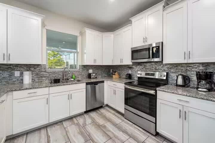 A kitchen features white cabinets, granite countertops, stainless steel appliances, and a gray tile backsplash — 9045 HAZARD STREET, DAVENPORT, FL