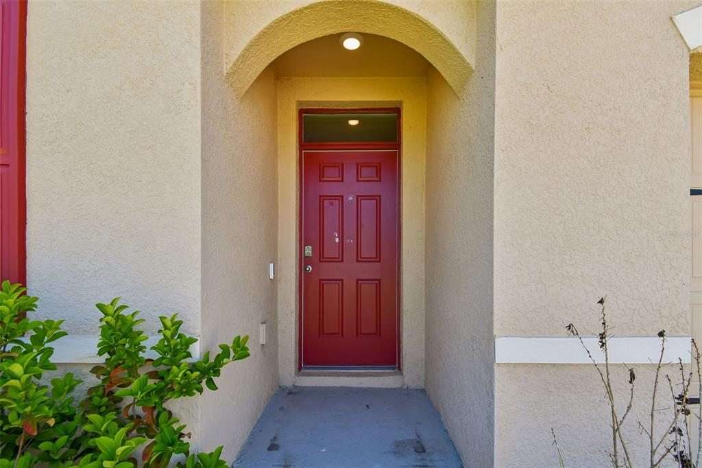 A red front door is set within a recessed entryway of a beige stucco home — 727 LAZIO CIRCLE, DEBARY, FL