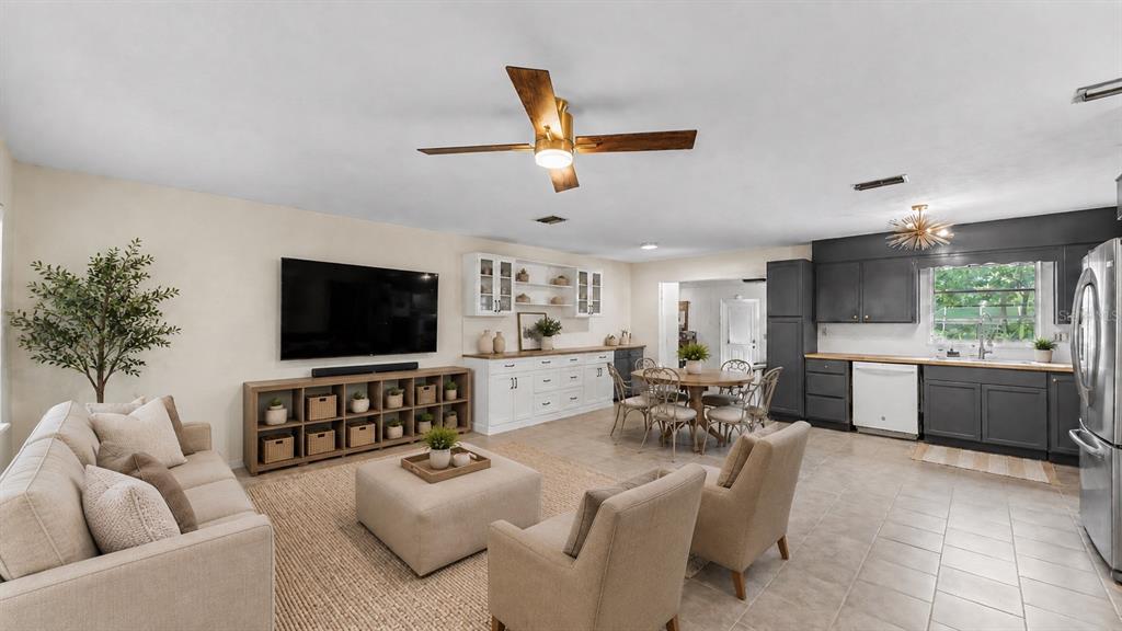 An open-concept living room and kitchen featuring neutral furniture, a wooden media console, and cabinetry — 7011 DAVIN STREET, LAKELAND, FL
