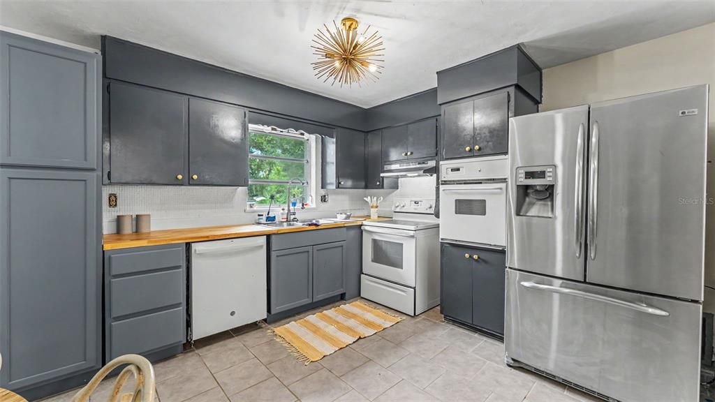A kitchen features grey cabinets, stainless steel appliances, a wood countertop, and a starburst chandelier — 7011 DAVIN STREET, LAKELAND, FL