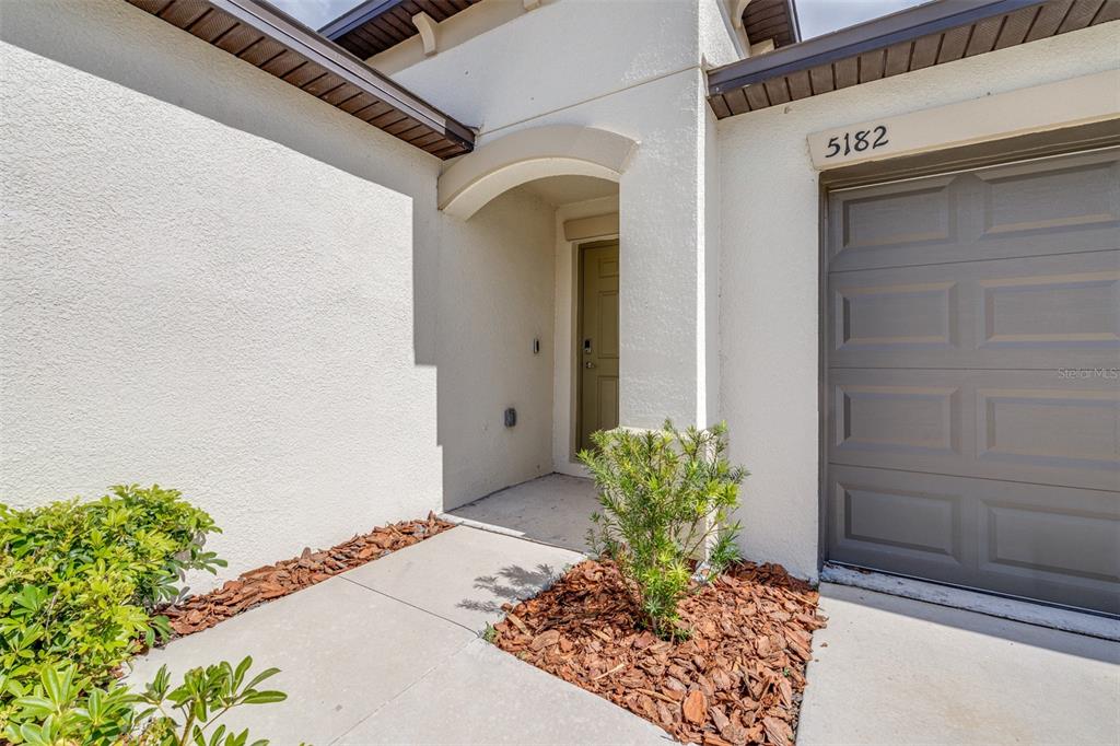 The exterior view shows a house entrance with a concrete walkway, landscaping, and a garage — 5182 FIDDLE FIG AVENUE, WIMAUMA, FL