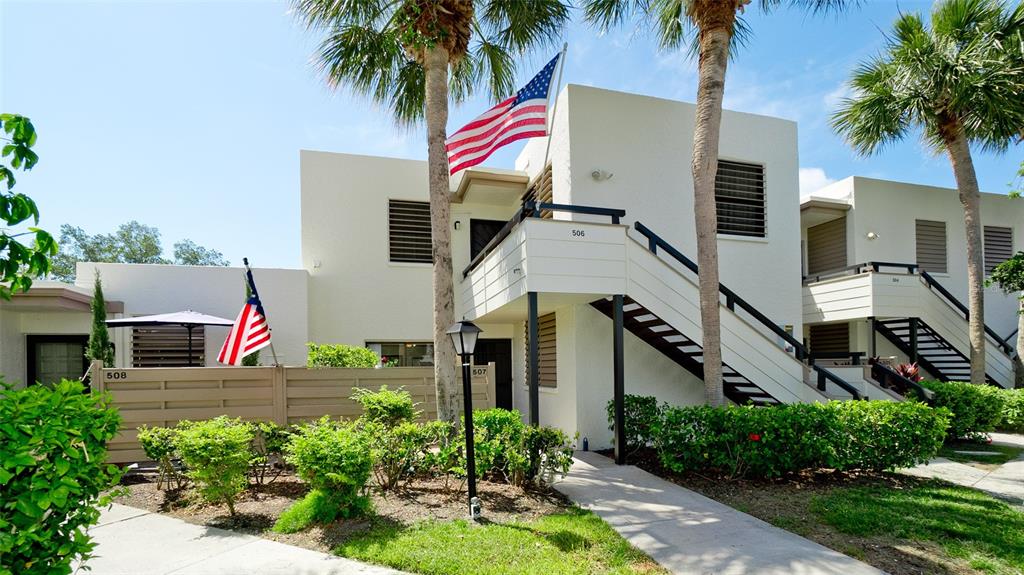 A two-story white stucco apartment building features exterior staircases and American flags — 507 LAKESIDE DRIVE UNIT 507, BRADENTON, FL