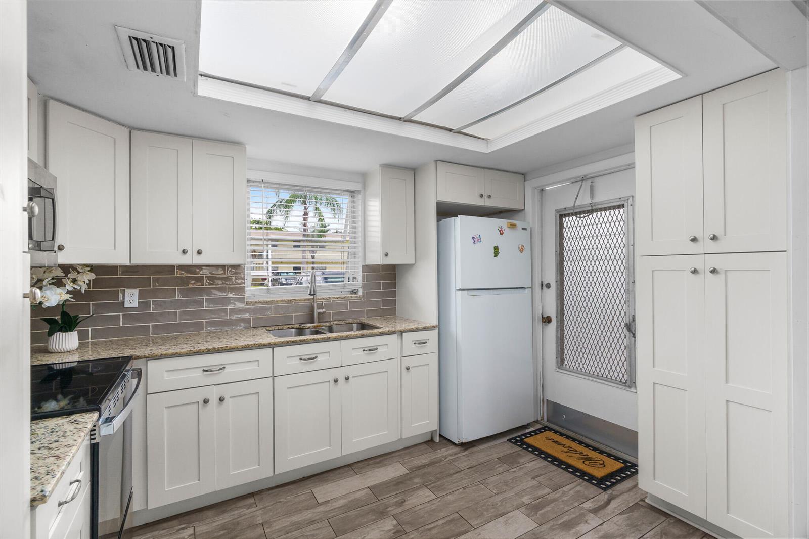 A kitchen features white cabinets, granite countertops, a tiled backsplash, and a white refrigerator — 410 NE 17th Avenue # 101, Boynton Beach FL 33435, BOYNTON BEACH, FL
