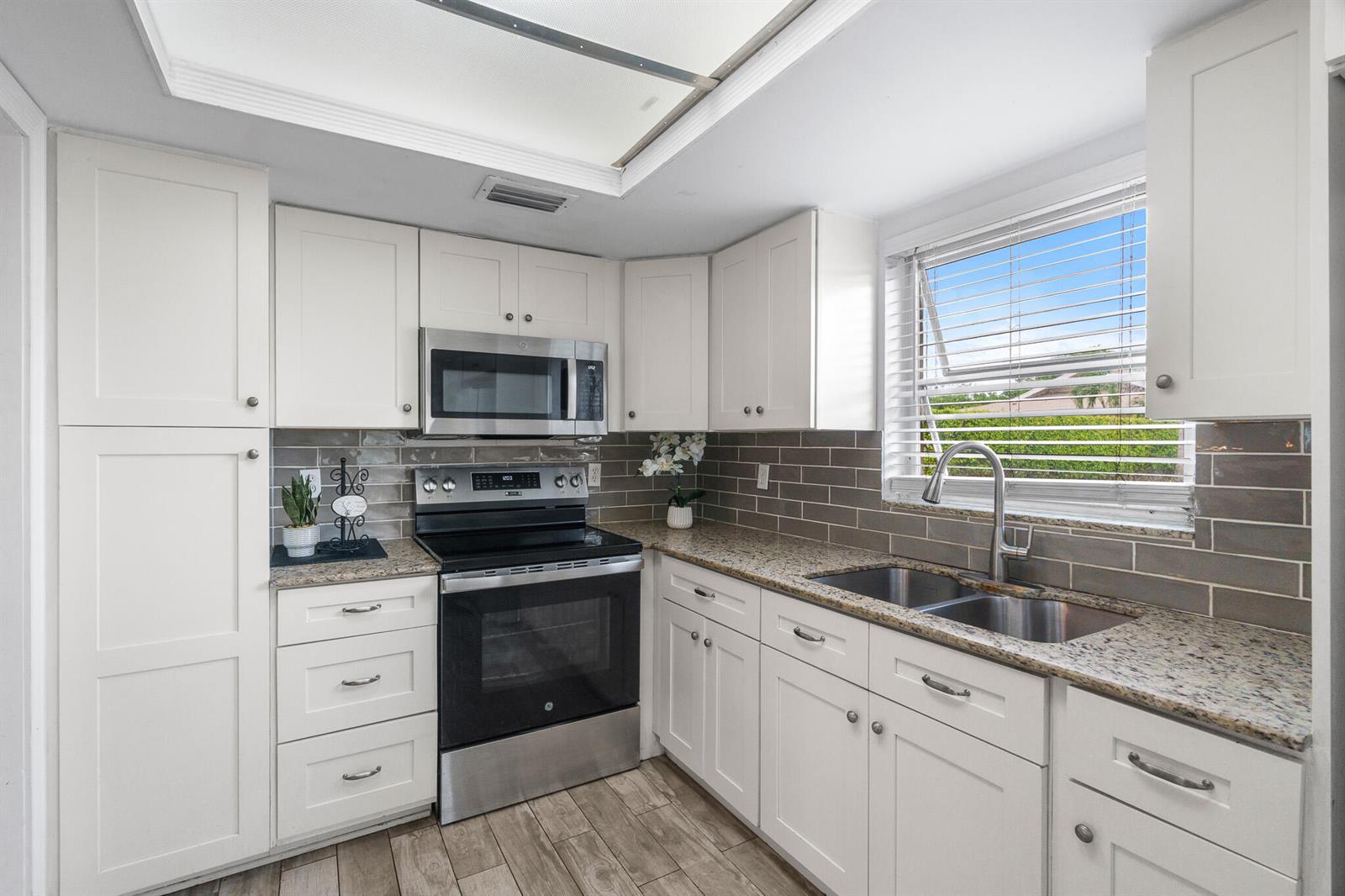 A kitchen features white cabinets, granite countertops, a stainless steel stove, and a subway tile backsplash — 410 NE 17th Avenue # 101, Boynton Beach FL 33435, BOYNTON BEACH, FL