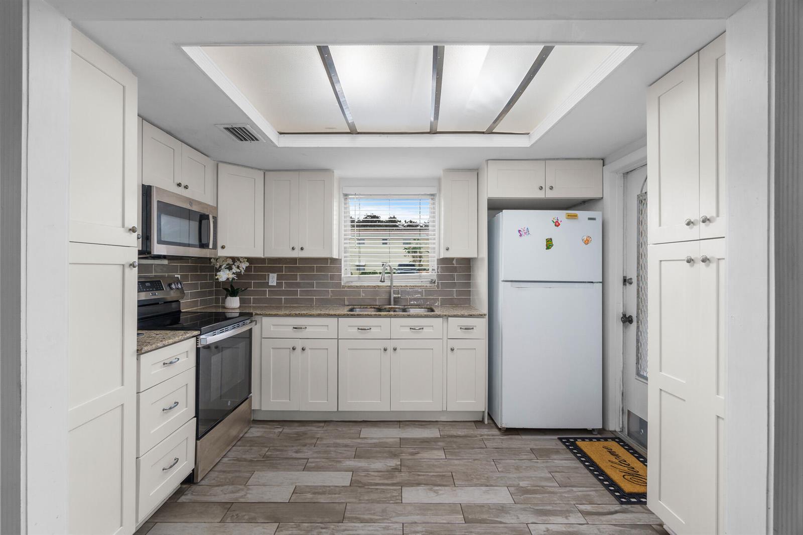 A kitchen with white cabinets, stainless steel appliances, a gray tile backsplash, and wood-look flooring — 410 NE 17th Avenue # 101, Boynton Beach FL 33435, BOYNTON BEACH, FL
