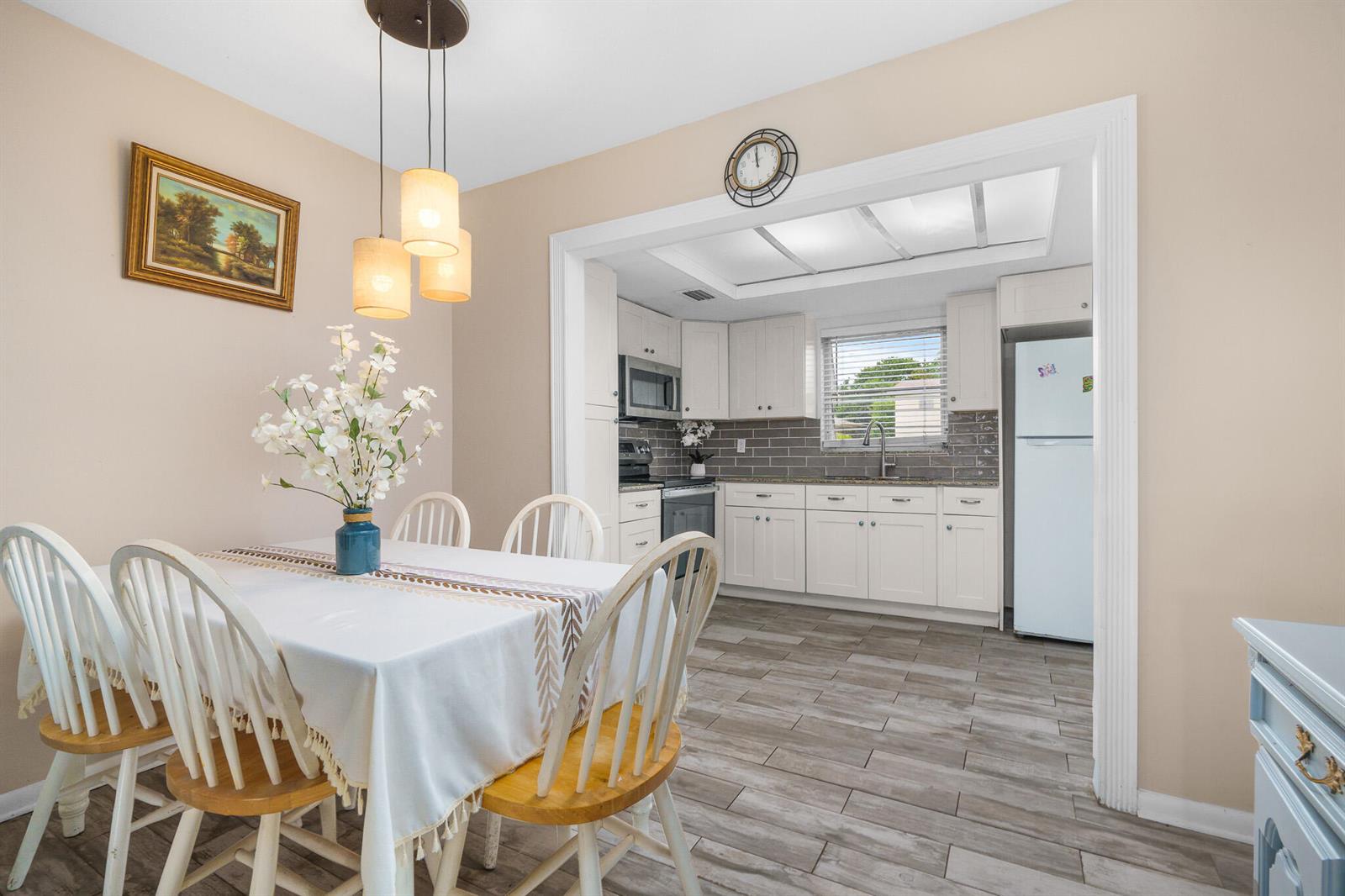 A dining area with a white table and chairs opens into a kitchen with white cabinetry — 410 NE 17th Avenue # 101, Boynton Beach FL 33435, BOYNTON BEACH, FL