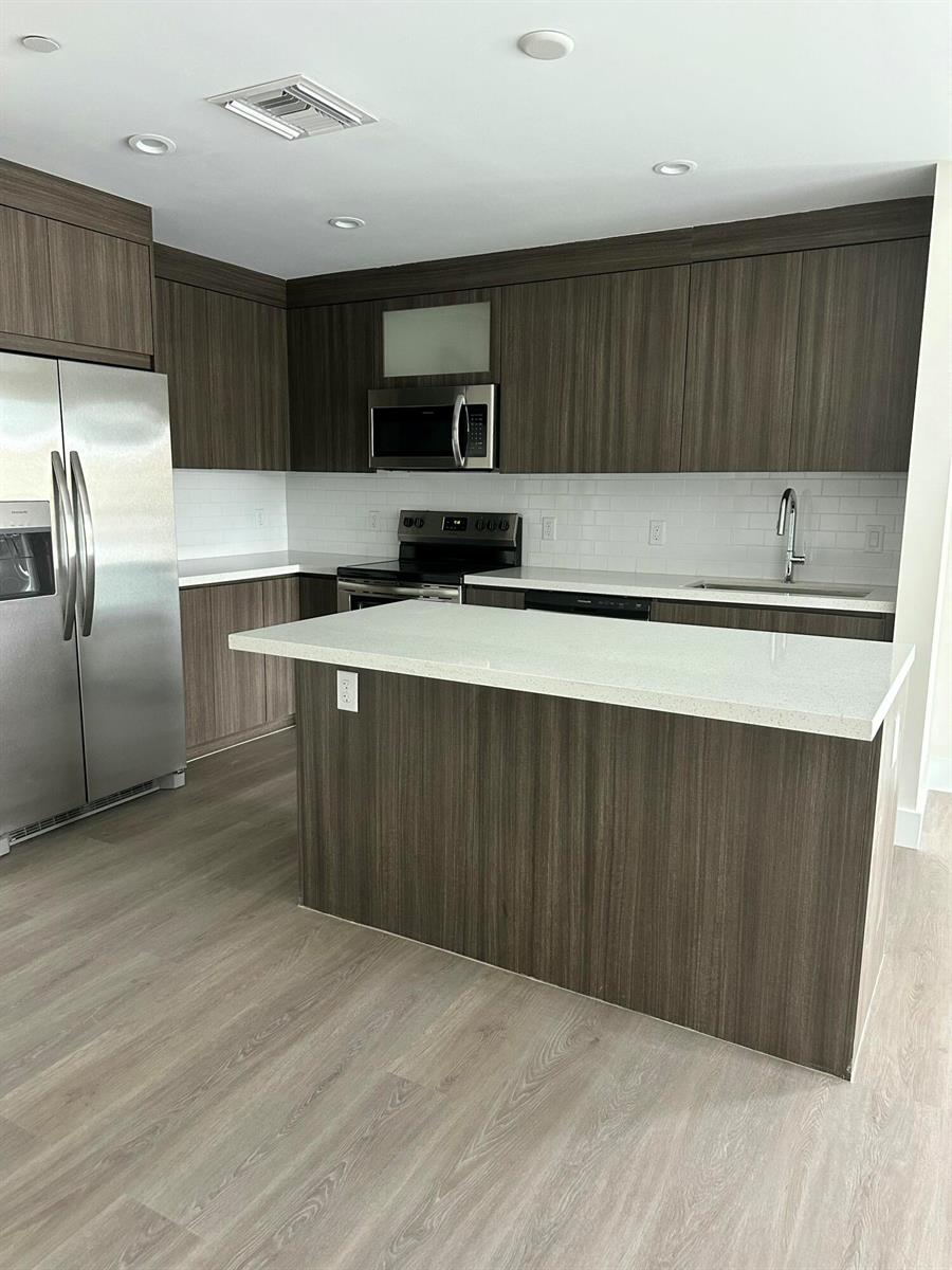 A modern kitchen features dark wood cabinetry, white countertops, stainless steel appliances, and light flooring — 1938 Jackson Street, Hollywood FL 33020, HOLLYWOOD, FL