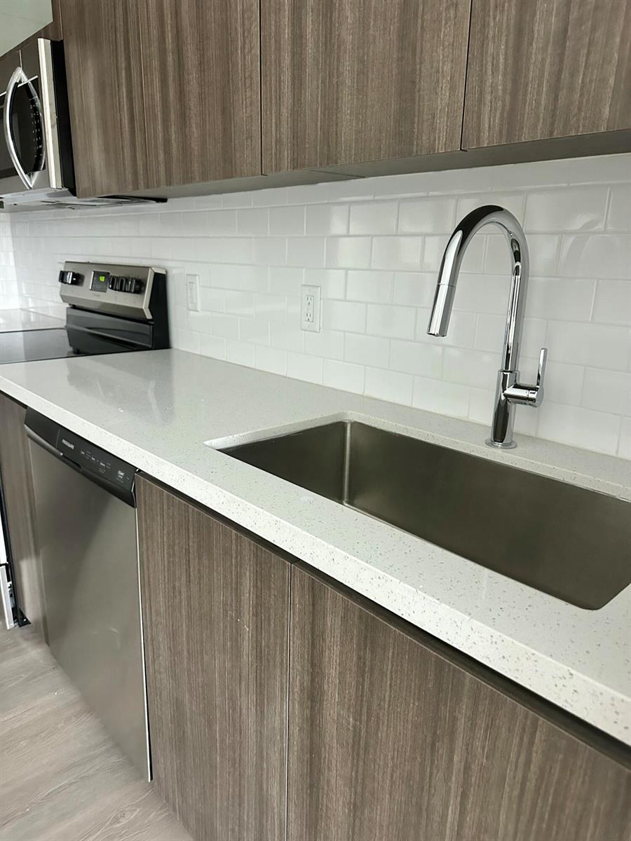 A modern kitchen features wood-grain cabinets, white quartz countertops, a stainless steel sink, and backsplash — 1938 Jackson Street, Hollywood FL 33020, HOLLYWOOD, FL
