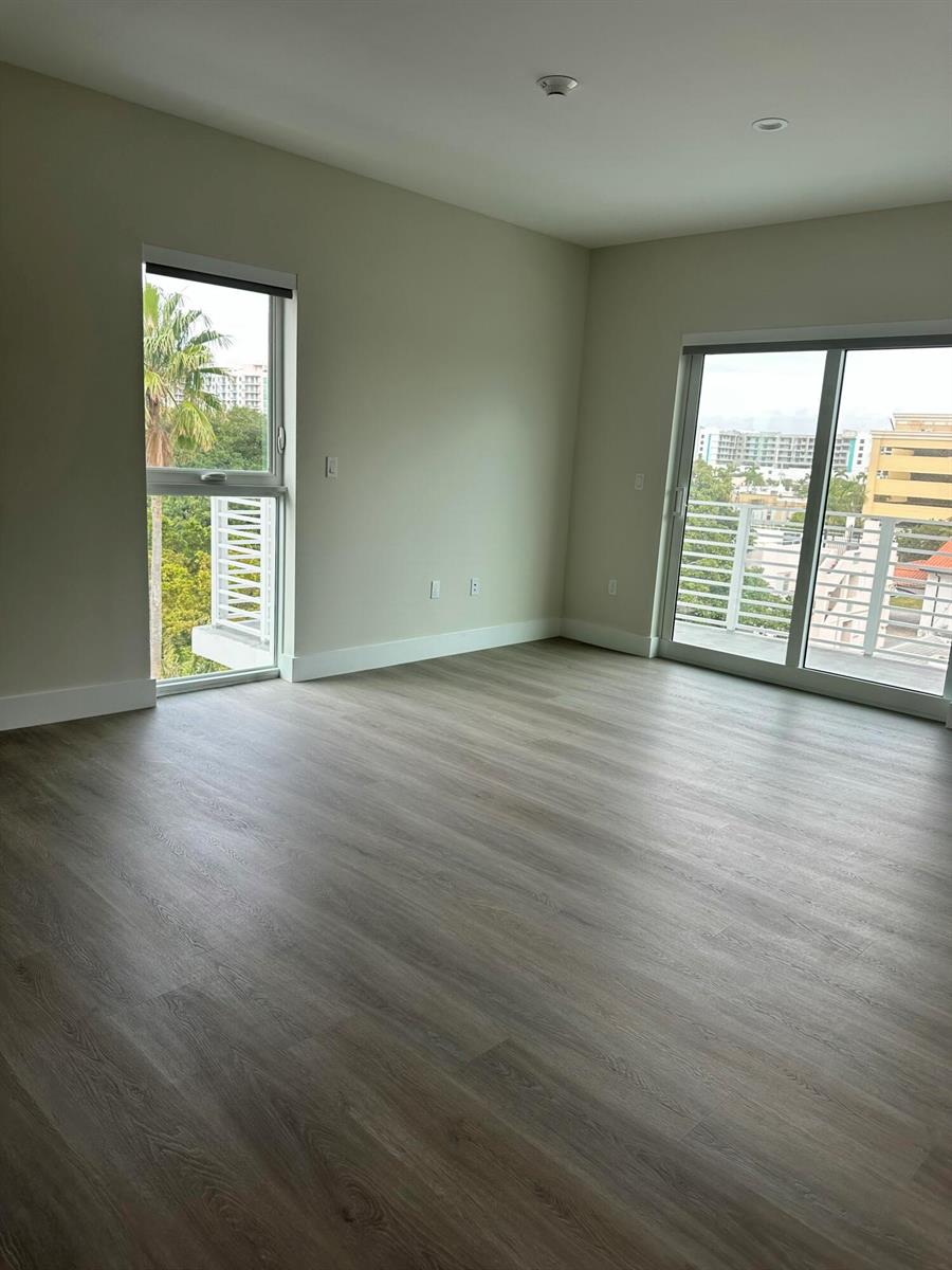 An empty room with light wood-look flooring, a tall window, and a sliding glass door — 1938 Jackson Street, Hollywood FL 33020, HOLLYWOOD, FL