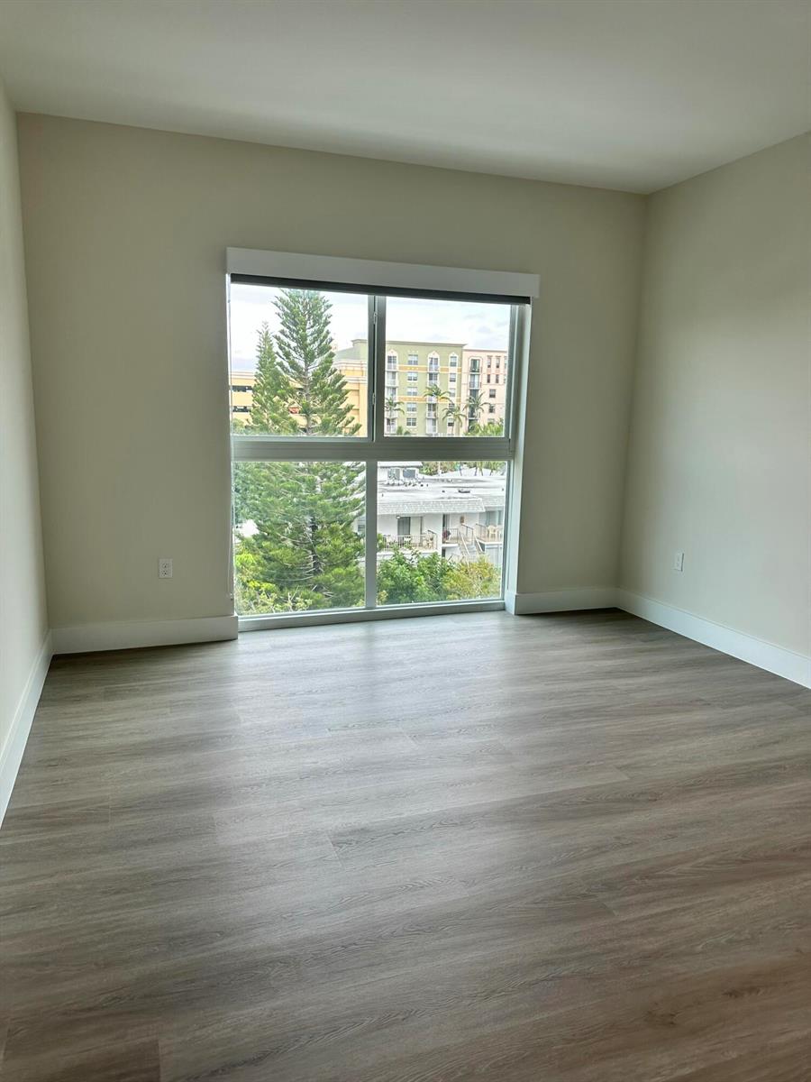 An empty room with light-colored walls, wood-look flooring, and a large window overlooking trees — 1938 Jackson Street, Hollywood FL 33020, HOLLYWOOD, FL