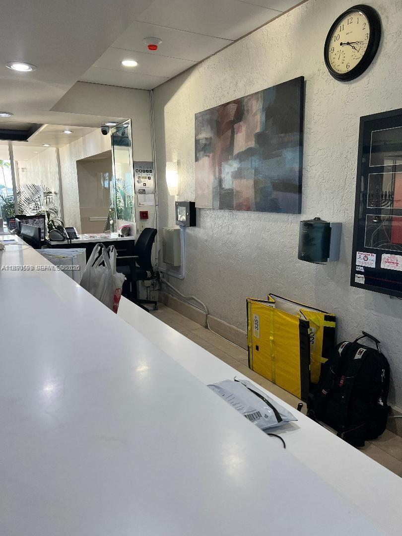 A reception area features a long white counter, wall art, a clock, and a backpack — 5005 Collins Ave # 322, Miami Beach FL 33140, MIAMI BEACH, FL