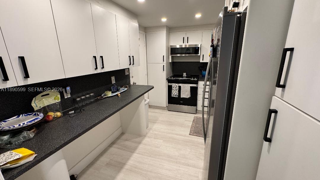 A kitchen features white cabinetry, black countertops, stainless steel appliances, and light wood-look flooring — 5005 Collins Ave # 322, Miami Beach FL 33140, MIAMI BEACH, FL