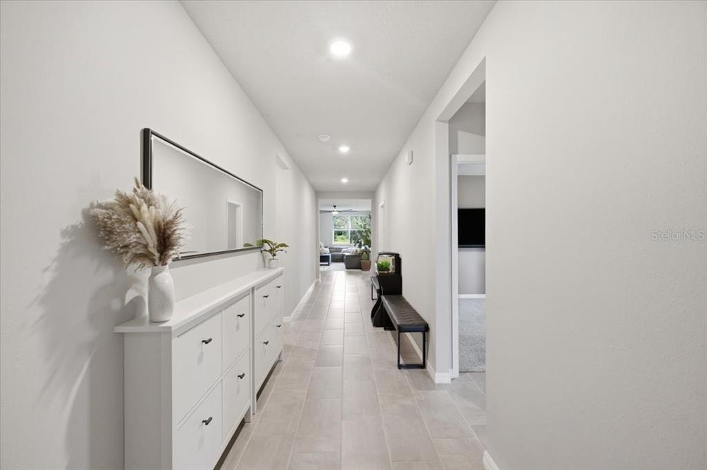 A long, white-walled hallway features light tile flooring, a shoe cabinet, and a large mirror — 10119 DAYBREAK GLEN, PARRISH, FL