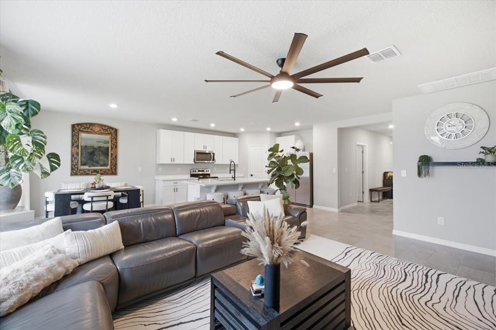 A living room with a grey sectional sofa, a coffee table, and an open kitchen — 10119 DAYBREAK GLEN, PARRISH, FL