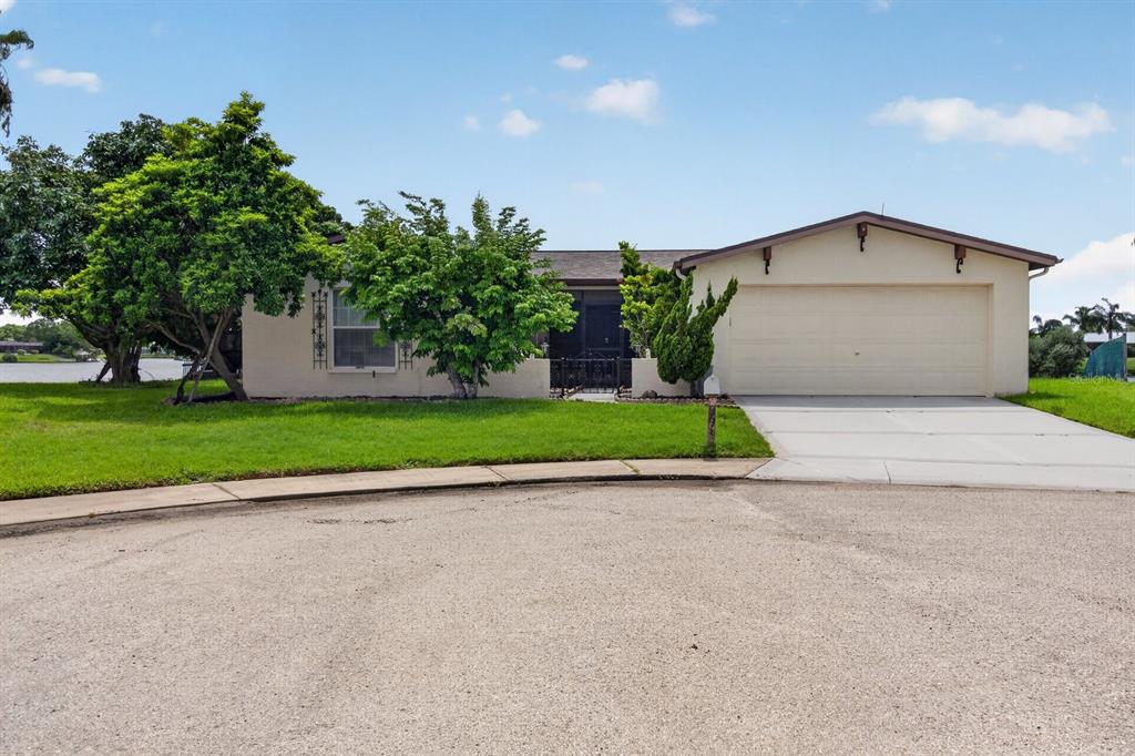 A single-story house with a two-car garage, a front lawn, and trees beside a lake — 9615 TOWANDA LANE, PORT RICHEY, FL