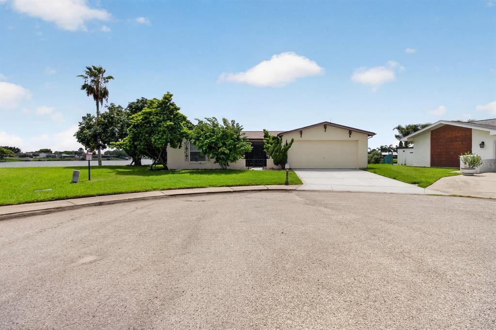 A single-story house with a two-car garage sits on a waterfront lot with green grass — 9615 TOWANDA LANE, PORT RICHEY, FL
