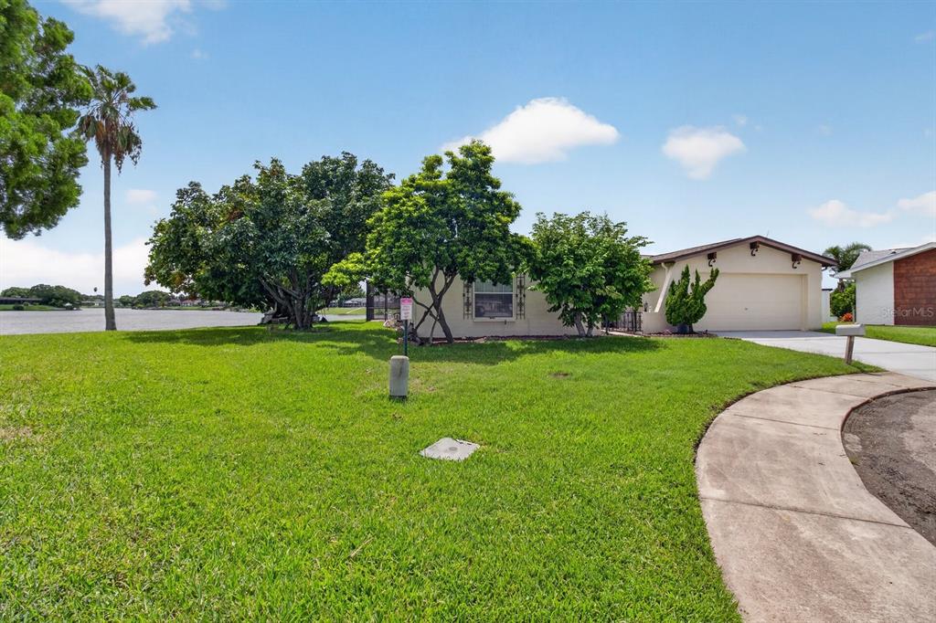 A single-story house with a two-car garage sits on a grassy lot by a lake — 9615 TOWANDA LANE, PORT RICHEY, FL