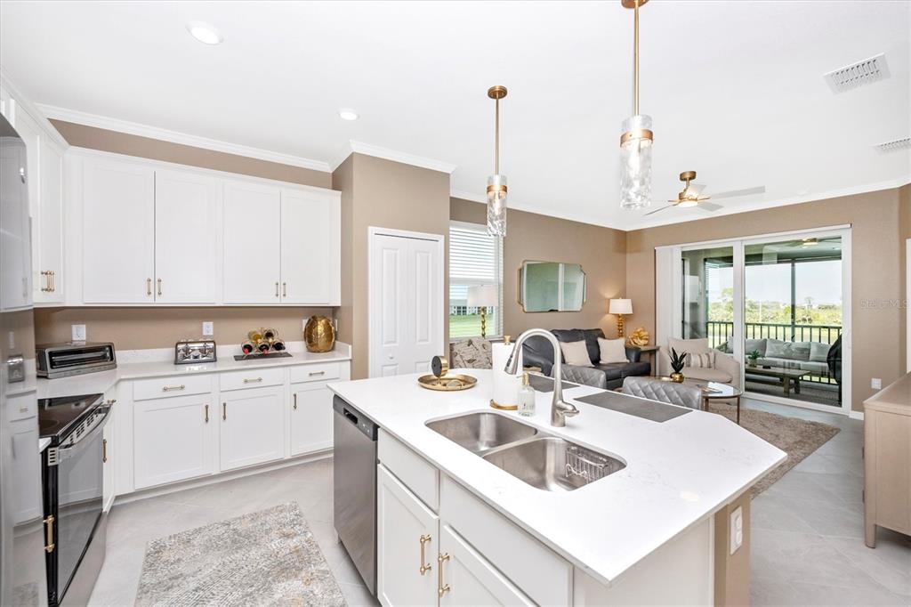 A kitchen with white cabinets, a central island with a sink, and an adjacent living area — 17625 OPAL SAND DRIVE UNIT 301, VENICE, FL