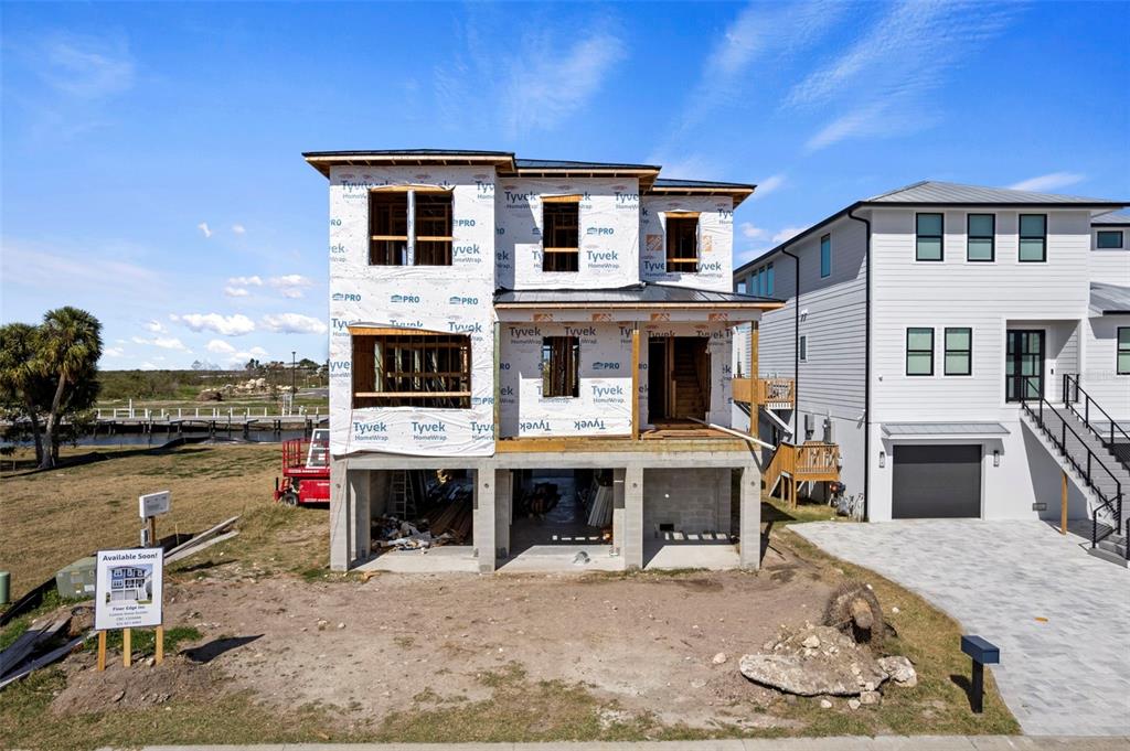 A three-story house under construction with Tyvek wrap stands next to a finished home — 5815 ELISABETHAN LANE, NEW PORT RICHEY, FL