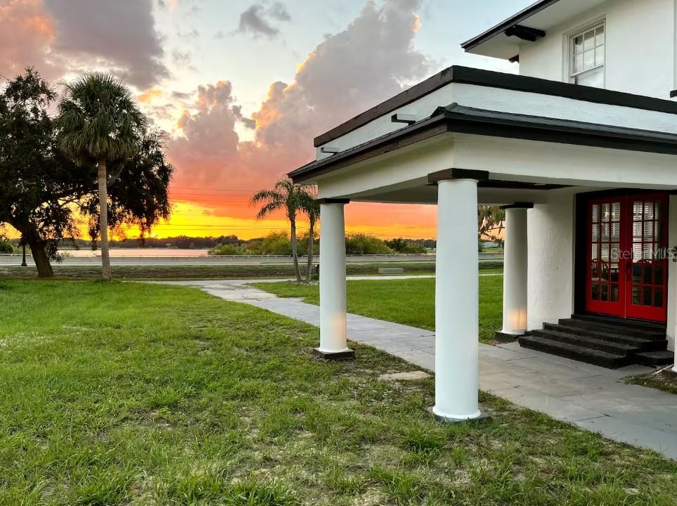 A white house with a columned porch overlooks a lake during a vibrant sunset — 1515 LAKE EVA CIRCLE, HAINES CITY, FL