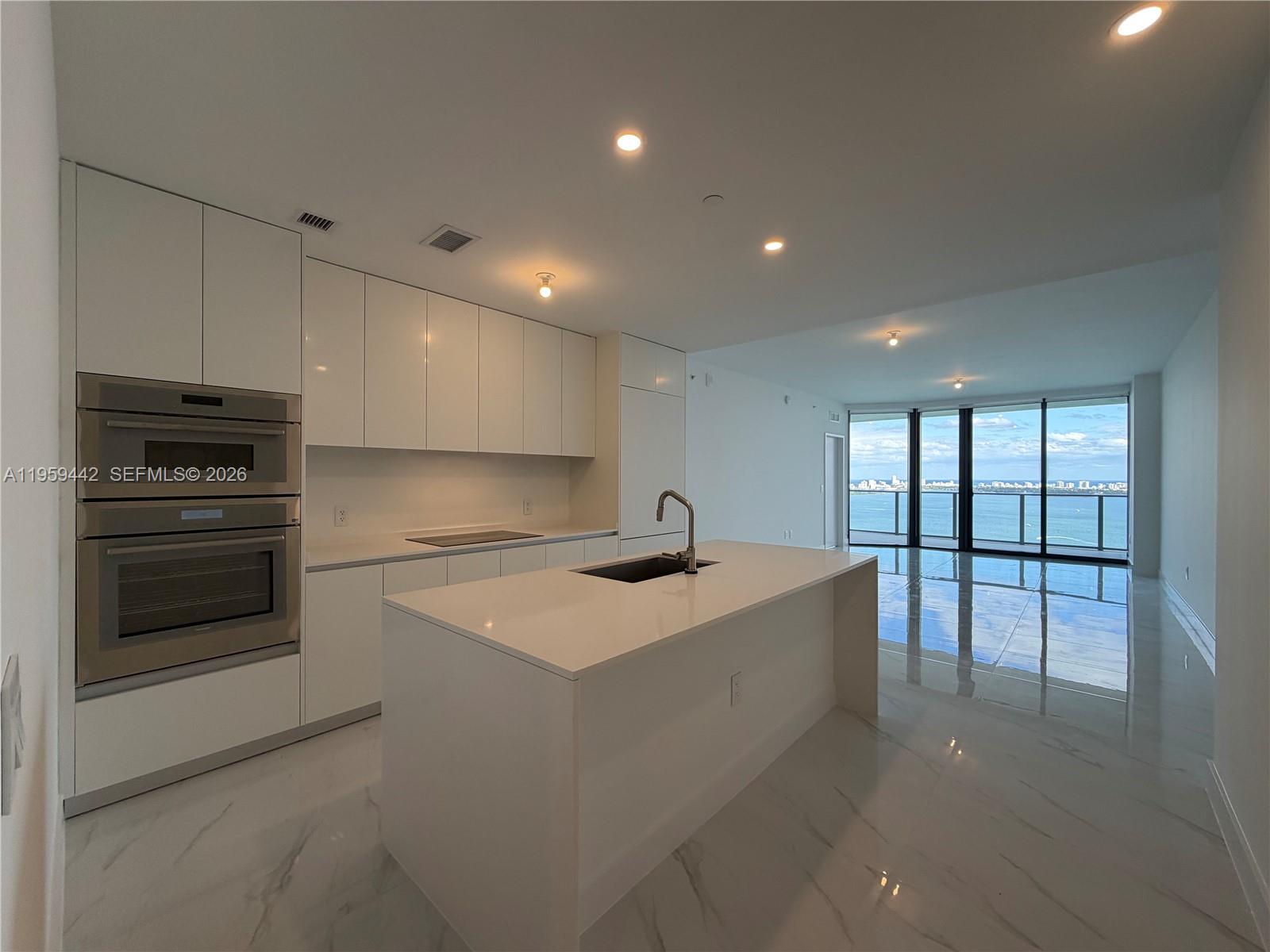 A modern kitchen features white cabinetry, a central island with a sink, and floor-to-ceiling windows — 700 ne 24 # 3503, Miami FL 33137, MIAMI, FL