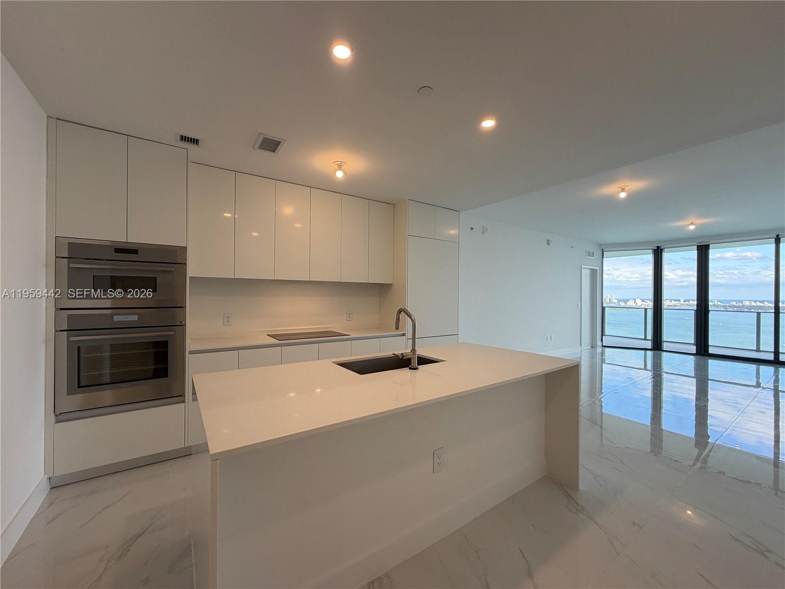 A modern kitchen features white cabinetry, a central island, and floor-to-ceiling windows overlooking water — 700 ne 24 # 3503, Miami FL 33137, MIAMI, FL
