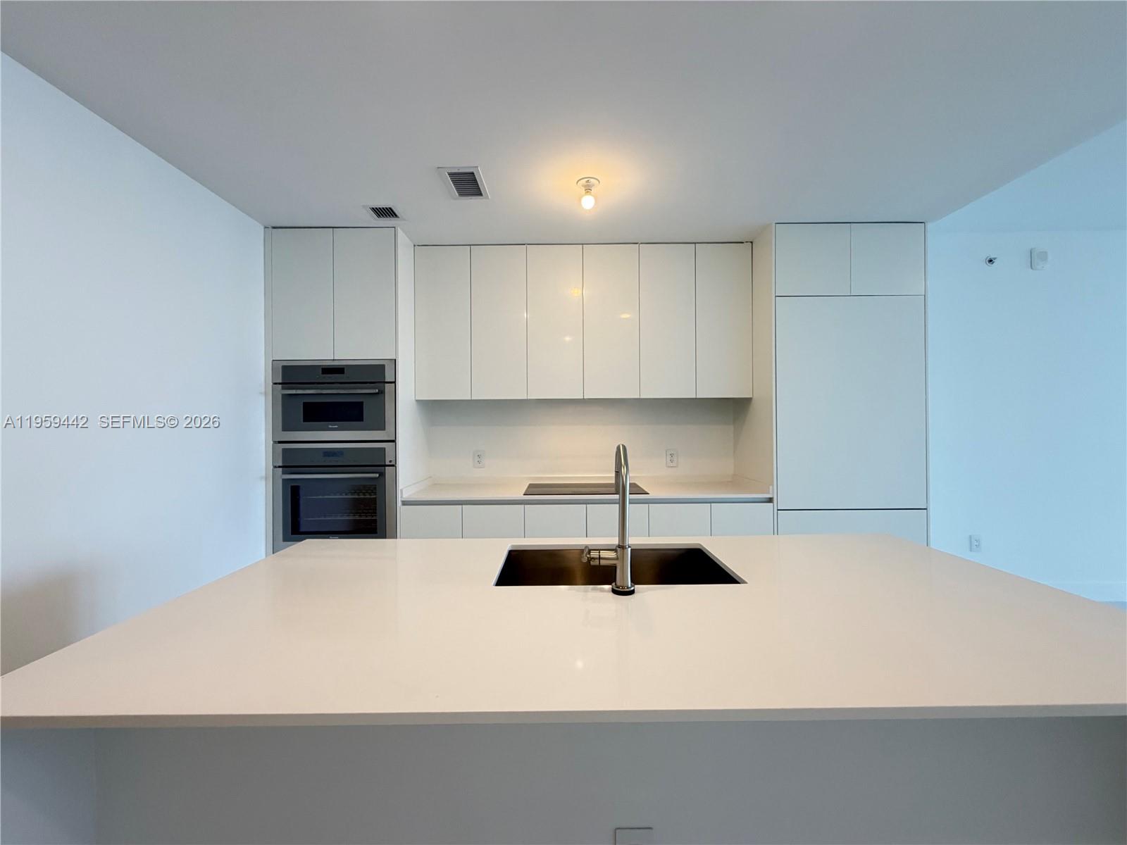 A modern kitchen features white cabinetry, a central island with a sink, and stainless appliances — 700 ne 24 # 3503, Miami FL 33137, MIAMI, FL