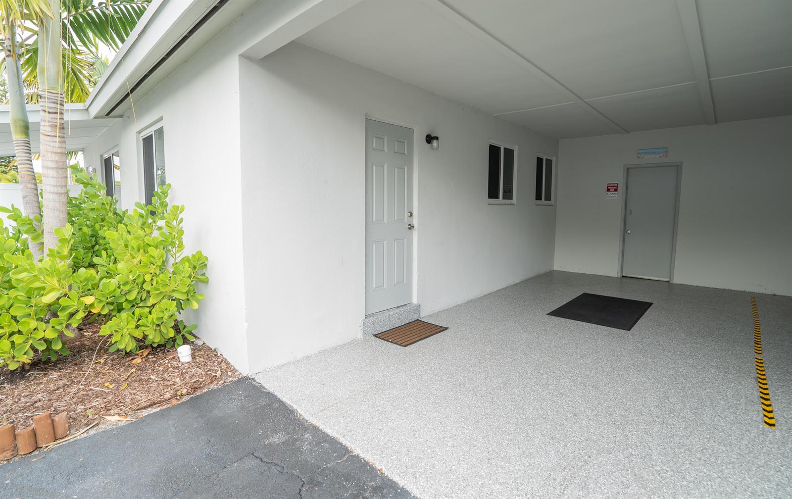 A covered carport with a grey speckled floor, two exterior doors, and a small bush — 1909 NE 2nd Street Unit 2, Pompano Beach FL 33060, POMPANO BEACH, FL