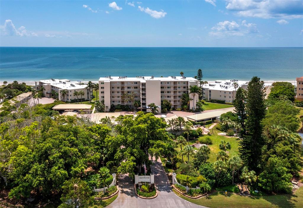 An aerial view shows a multi-story apartment building situated on a beach with lush landscaping — 4825 GULF OF MEXICO DRIVE UNIT 105, LONGBOAT KEY, FL