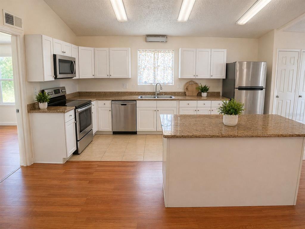 A kitchen features white cabinets, stainless steel appliances, a granite island, and wood-look flooring — 1446 NW MAGNOLIA TERRACE, ARCADIA, FL