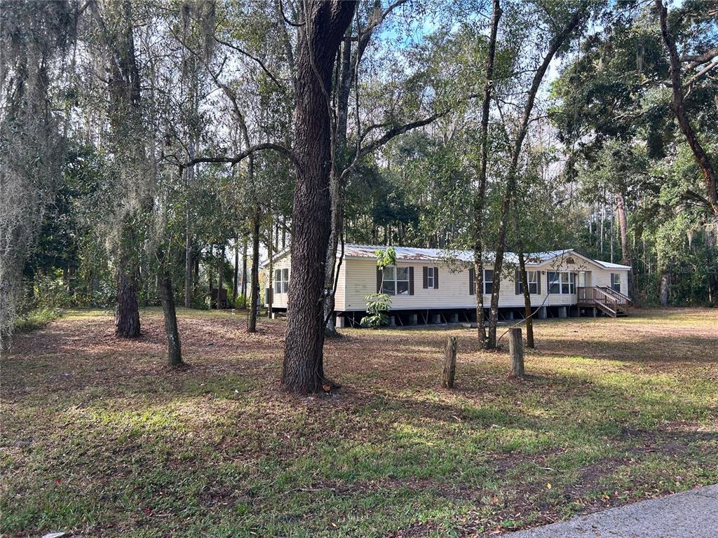 A manufactured home sits on a wooded lot with a raised foundation and wooden deck — 9867 JEROME DRIVE, NEW PORT RICHEY, FL
