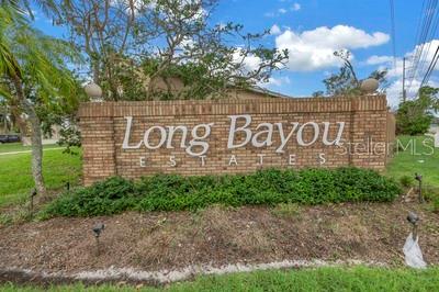 A brick monument sign displays the name Long Bayou Estates in a grassy outdoor area — 7380 PEBBLE BEACH LANE, SEMINOLE, FL